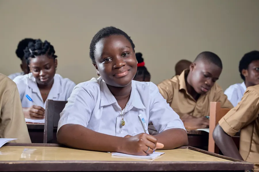 A smiling schoolgirl writing at her desk in class