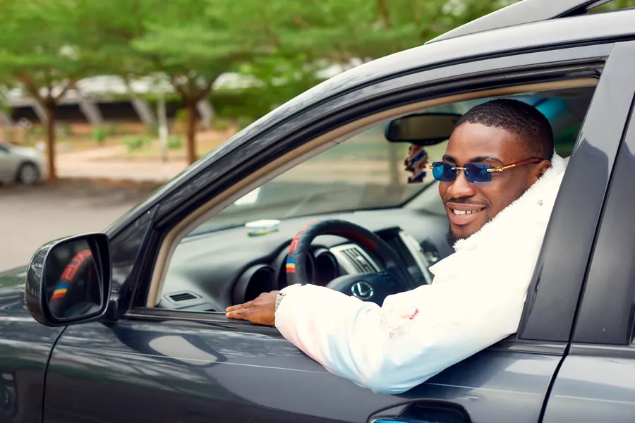 A smiling man in sunglasses at the wheel of his car
